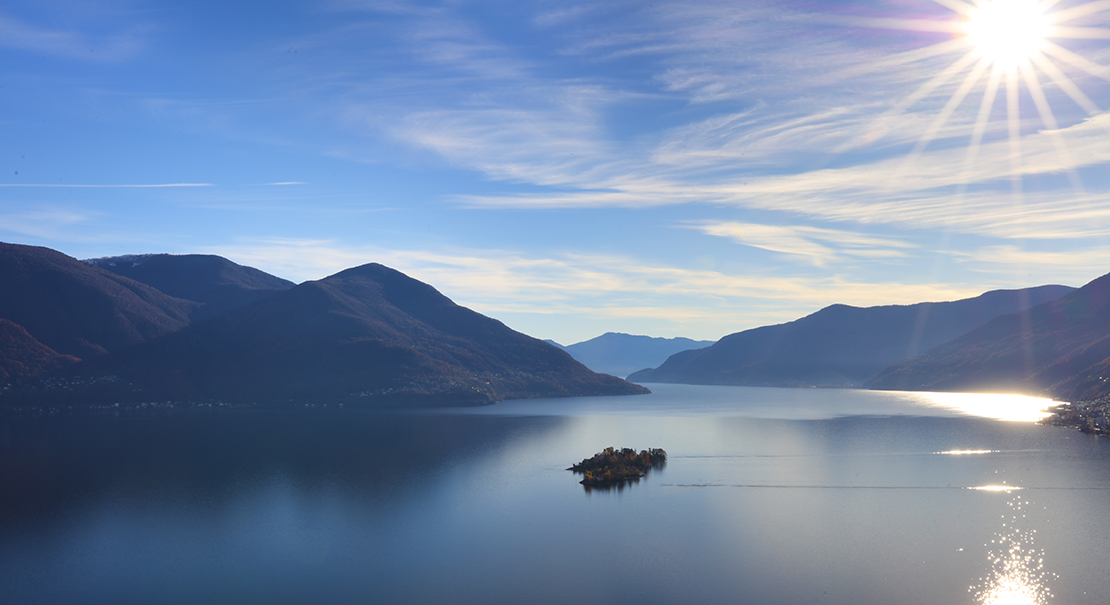 Sunlit aerial view of Lago Maggiore with a small island and mountain ridges