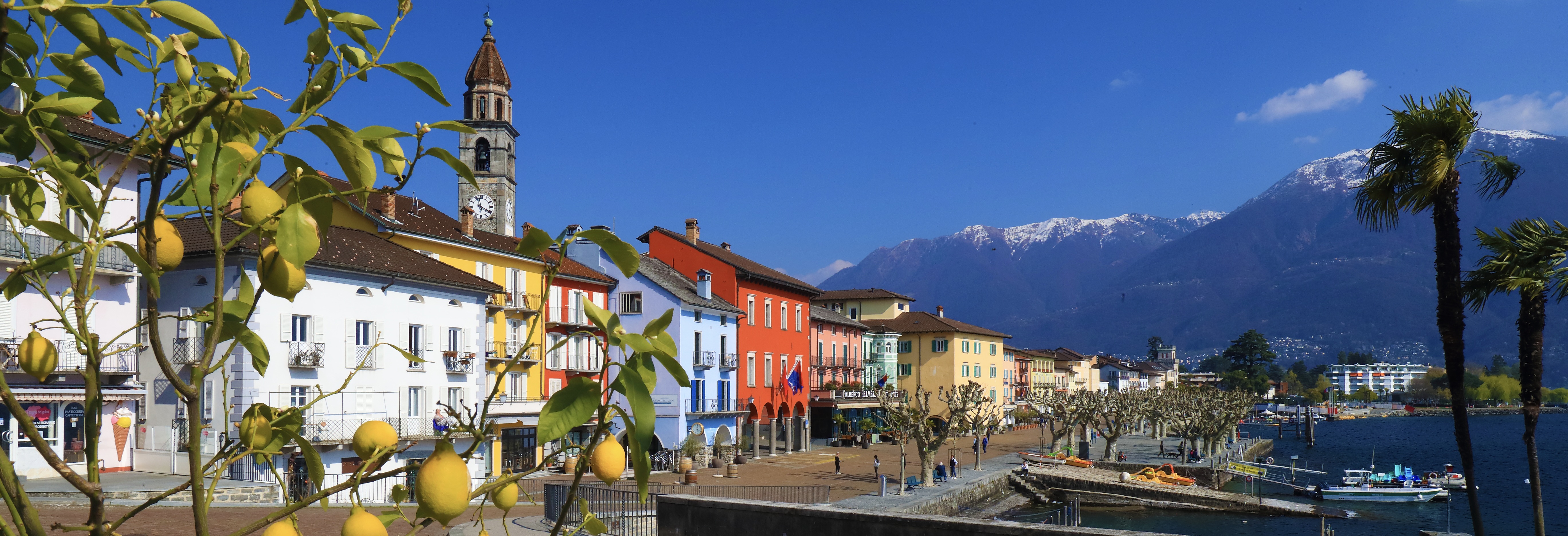 Colorful waterfront buildings and church tower in Ascona with snow-capped mountains behind