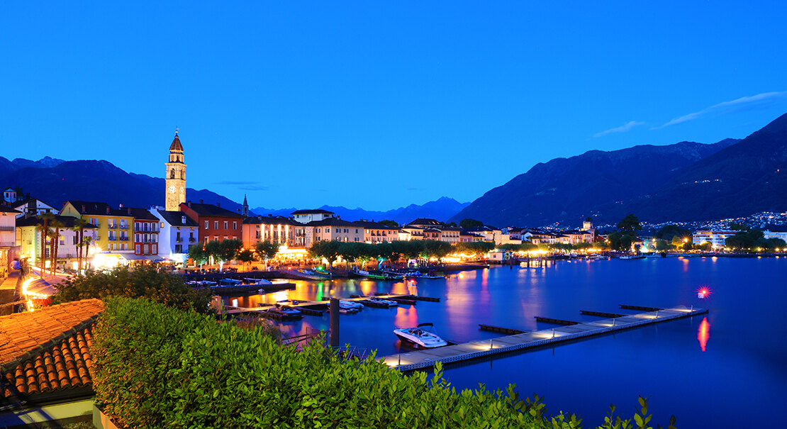 Evening view of Ascona's waterfront with the church tower and lights reflected on the lake